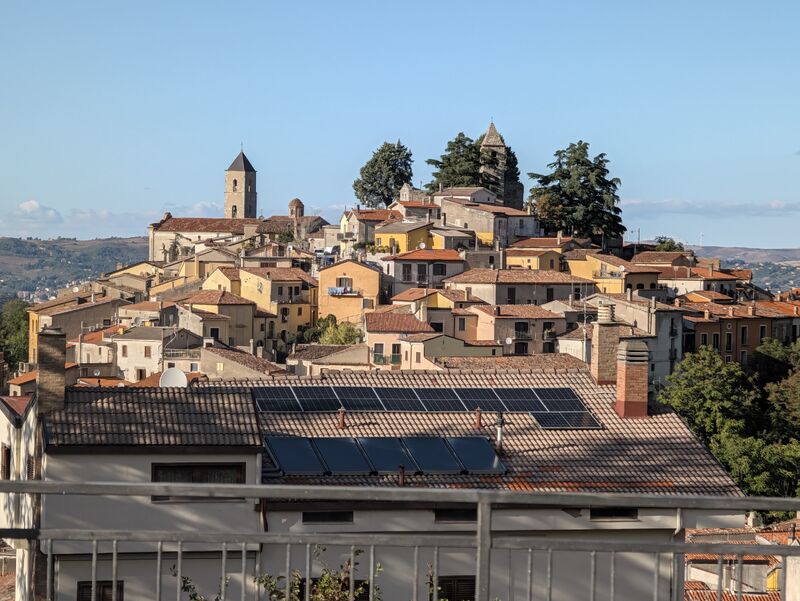 Un borgo su una collina, con tetti in terracotta e un campanile, e pannelli solari su un tetto in primo piano