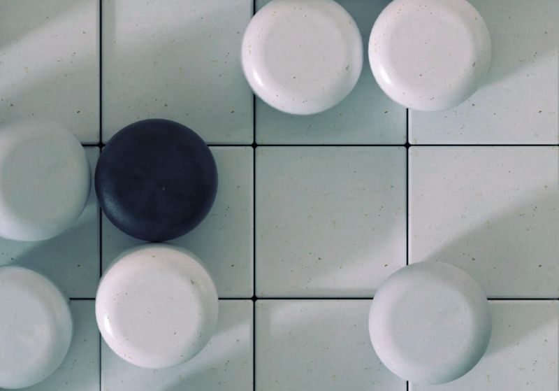 Close-up of a Go board with a single black stone surrounded by white stones